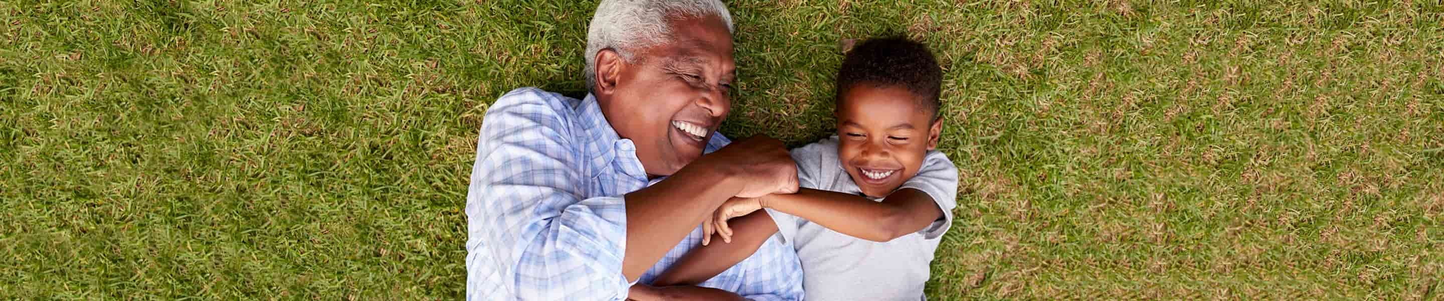 Grandfather and grandson laughing while laying on the grass.