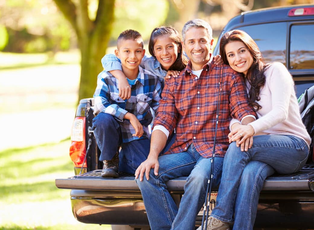 Family sitting in the back of a pickup truck on camping trip.