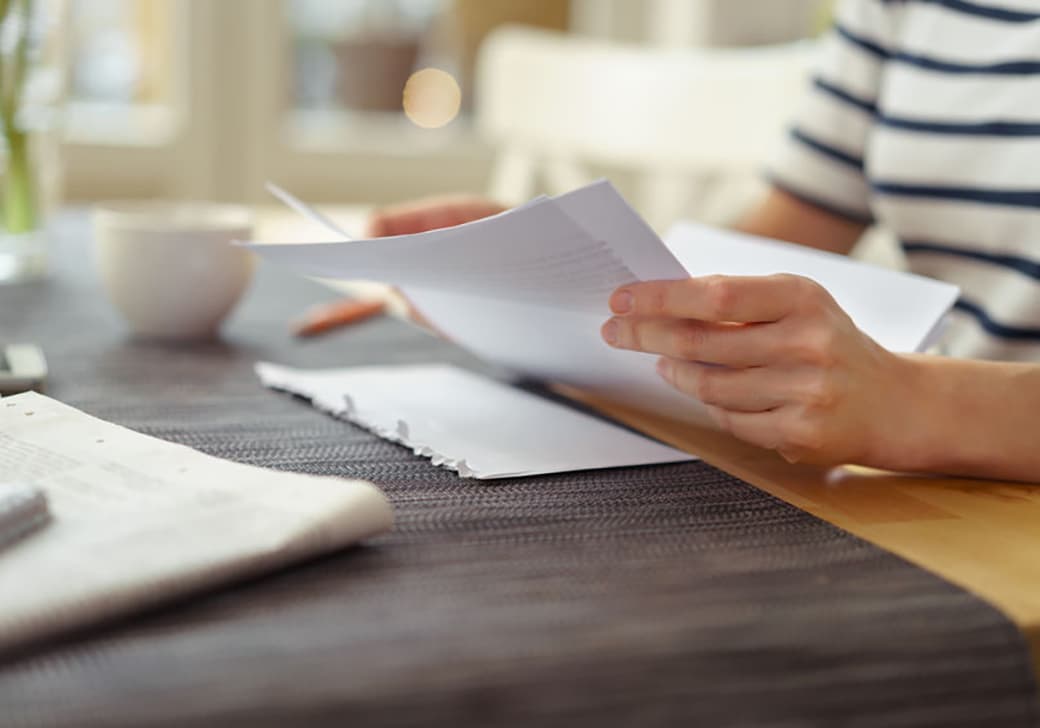 A person sitting at a table reading documents with a cup of coffee.