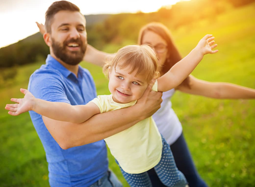 Father, mother, and daughter playing airplane in a grass field