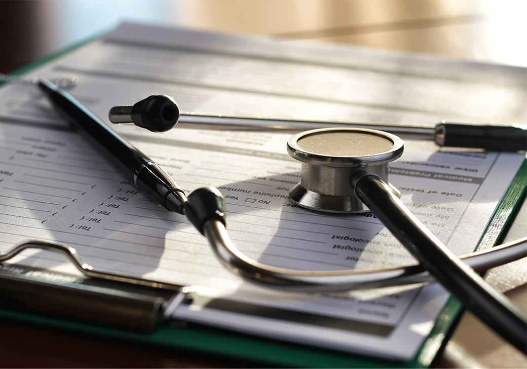 A pen and a stethoscope on top of a green clipboard with patient information document on a table.