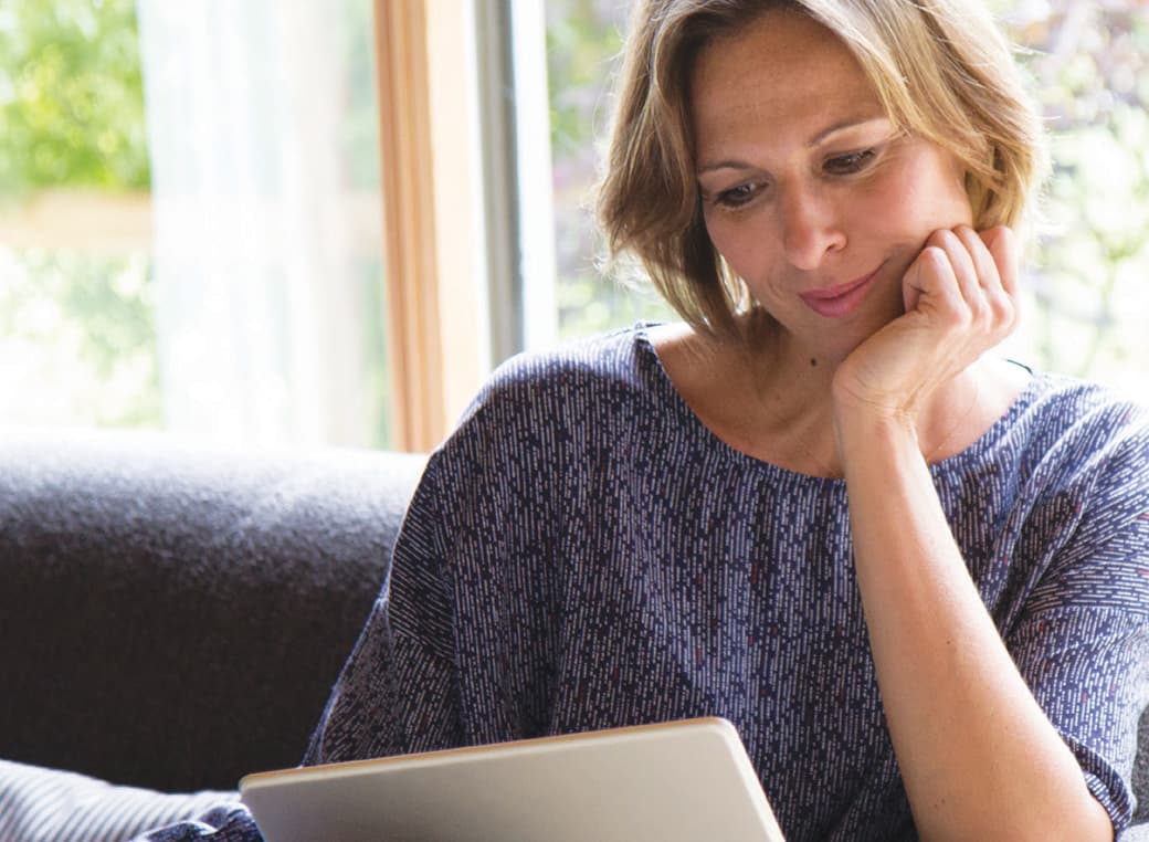 Woman sitting on a couch viewing a tablet.