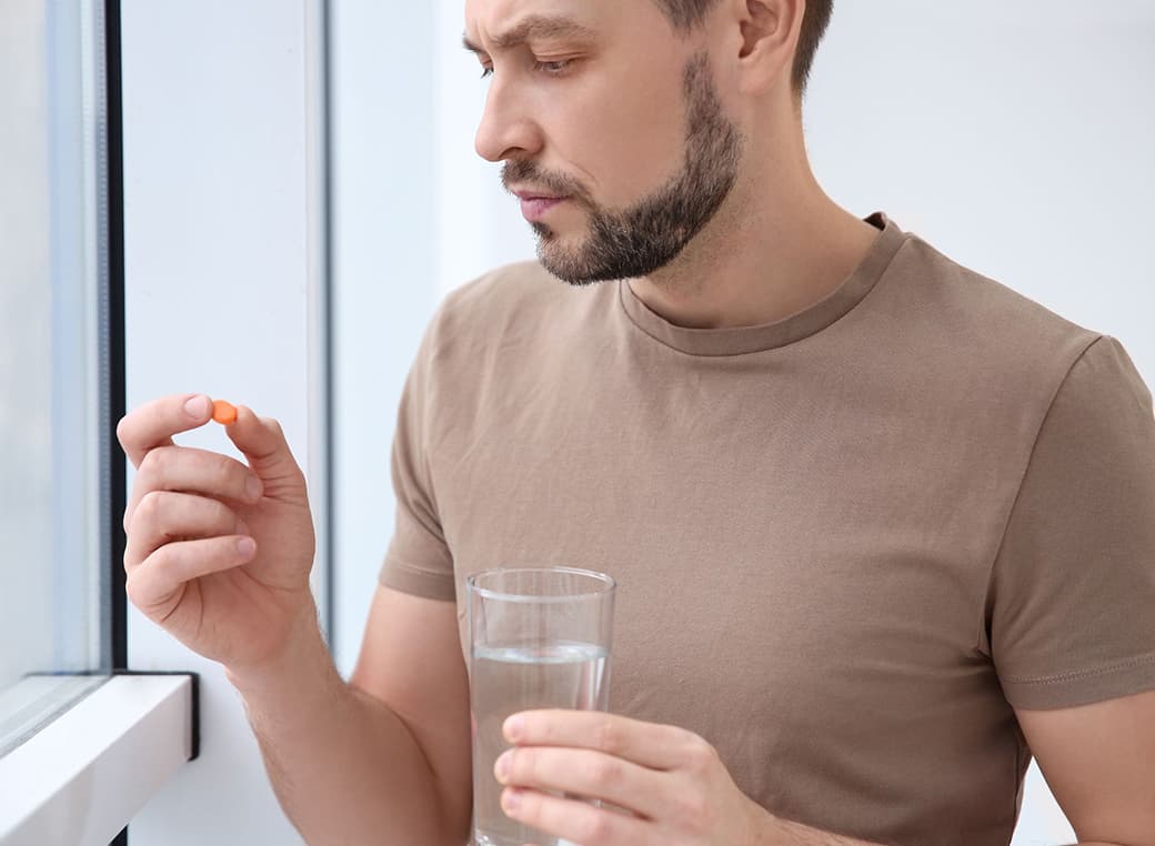 Man holding a cup of water and an antibiotic pill.