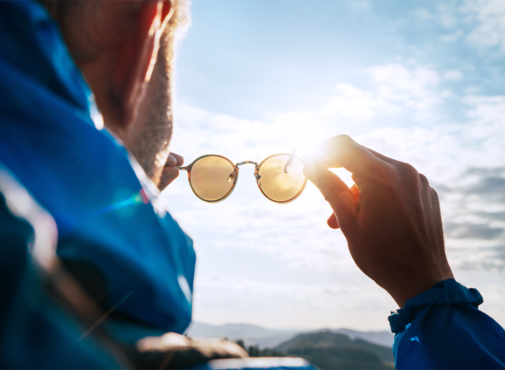 Back-hand shot of a man about to place his sunglasses on his face to protect his eyes from the sun.