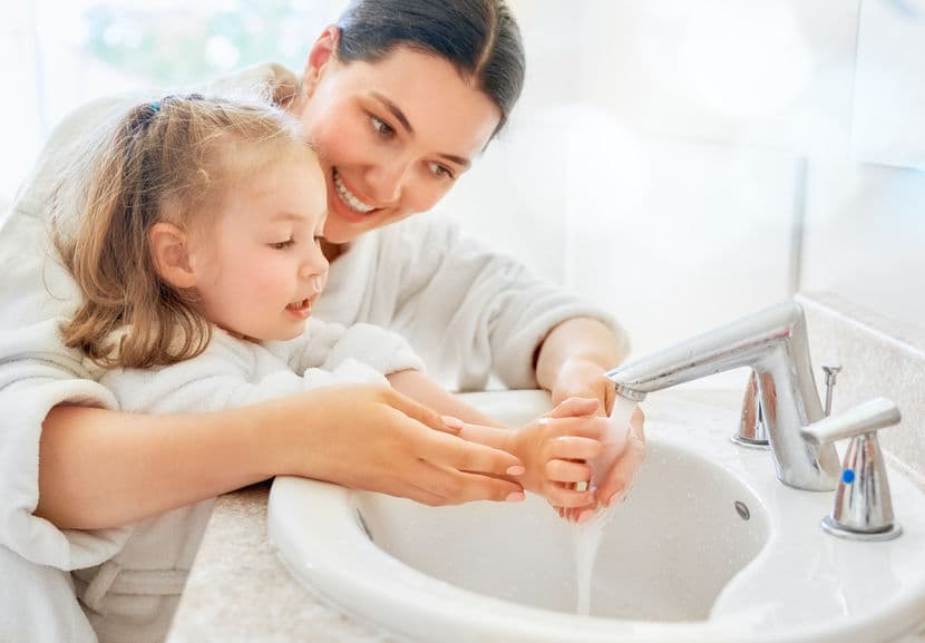 A mother helping her daughter wash her hands.