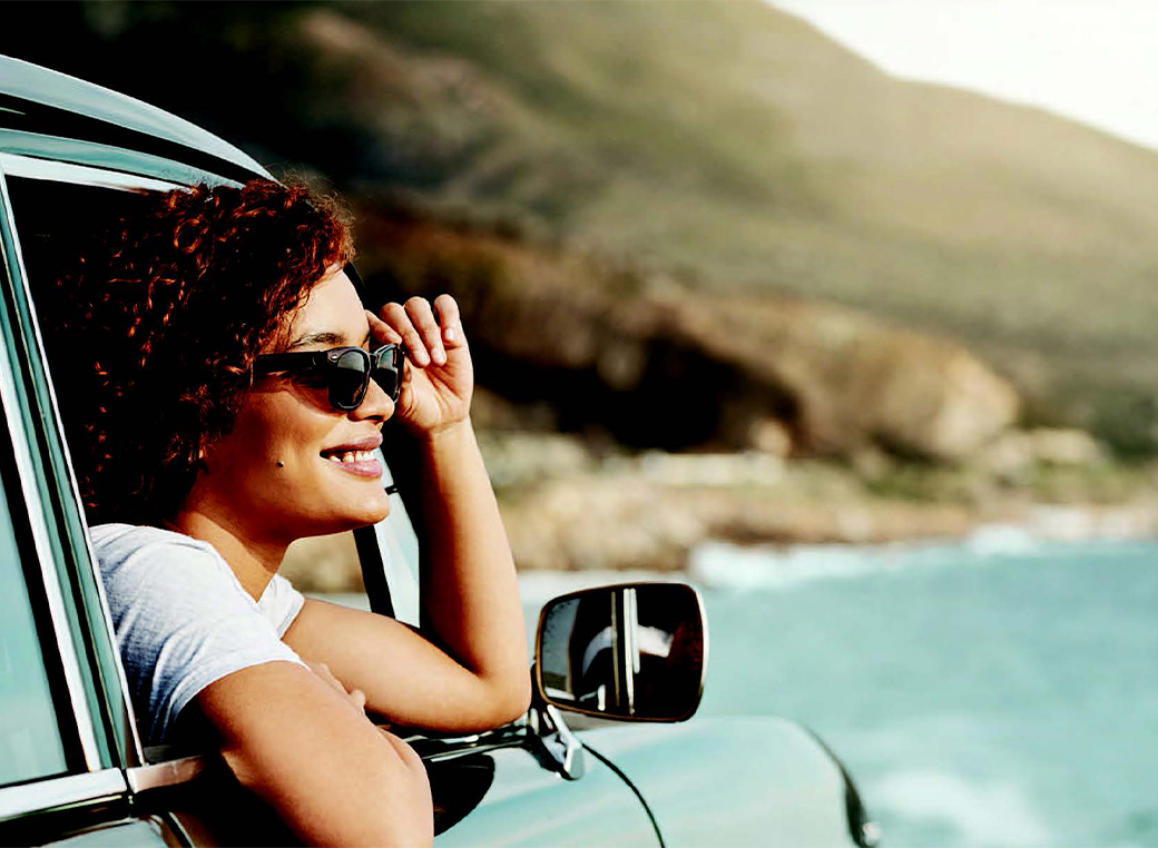 A younger woman starring out of a car where the background is a beach scenery.