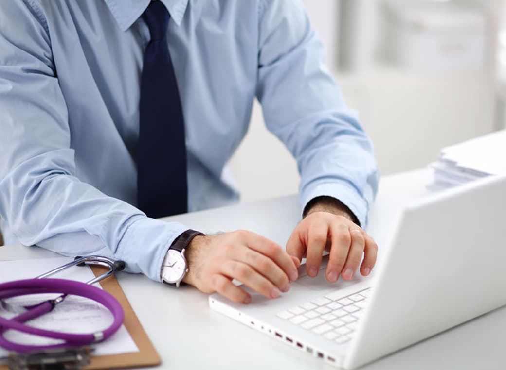 Provider sitting at a desk while typing on a laptop .