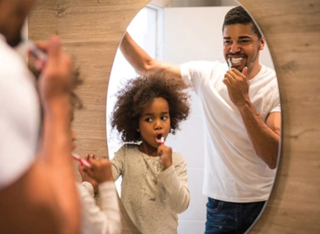 Father and son brushing their teeth together.