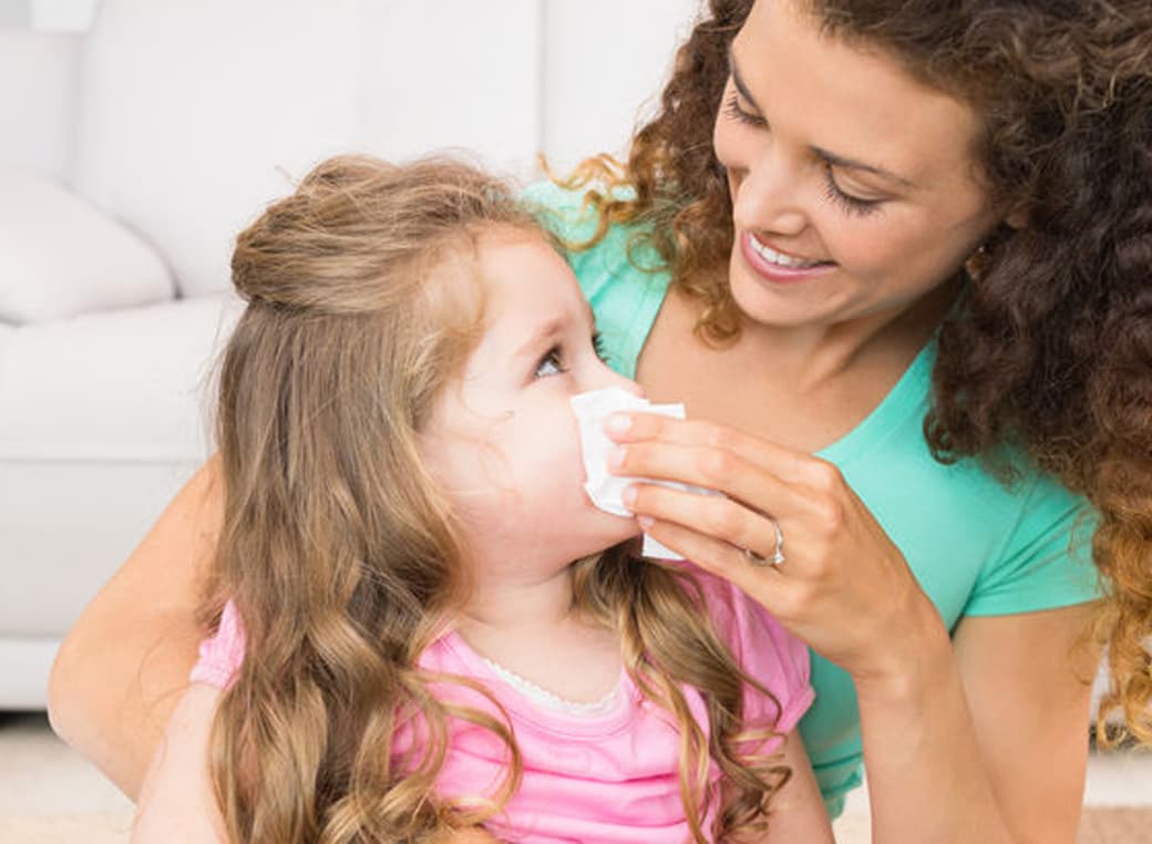 Mother helping her young daughter blow her nose in living room