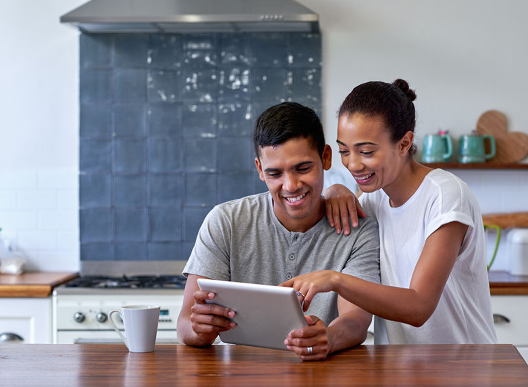 Couple enjoying morning coffee with tablet computer in kitchen at home