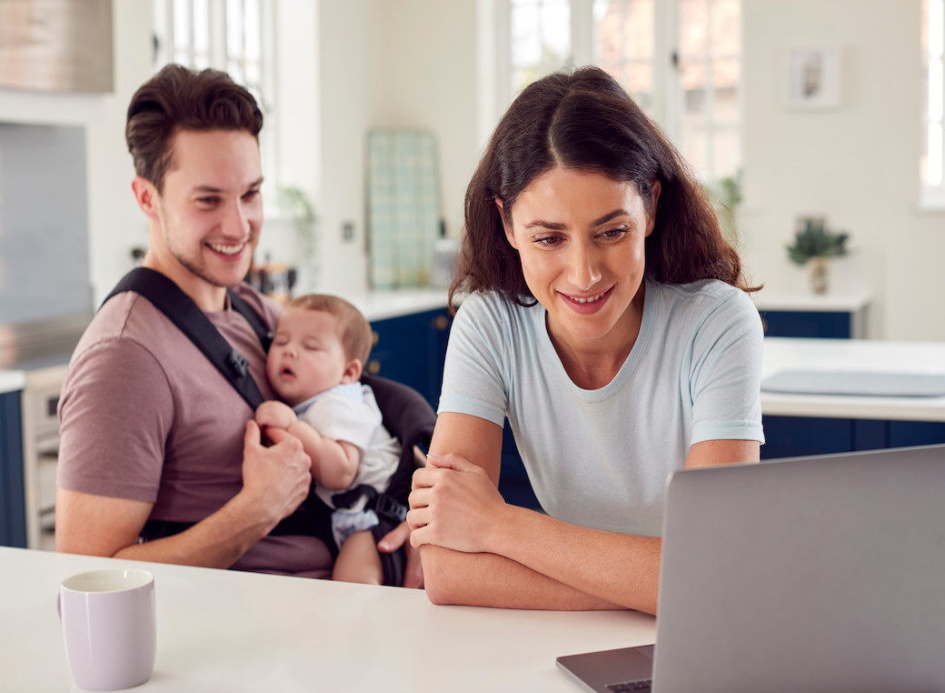 A younger family with a baby sitting at the kitchen in front of their computer.