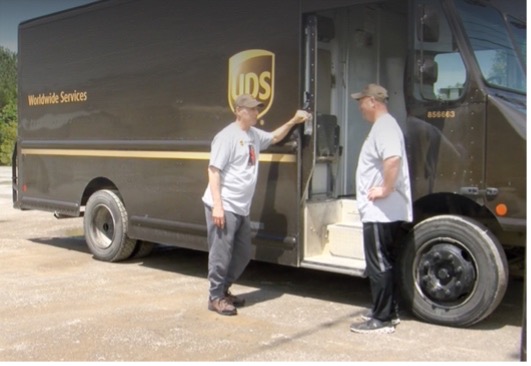 A UPS truck with two workers leaning up against the vehicle.
