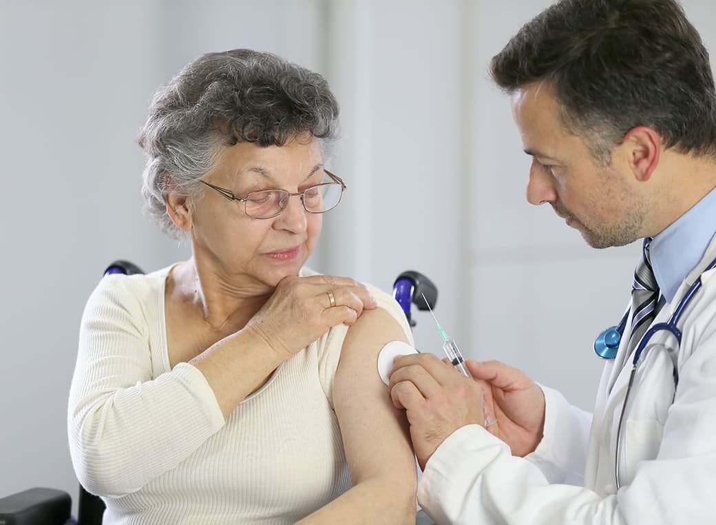 Male doctor administering flu shot to woman in an office.