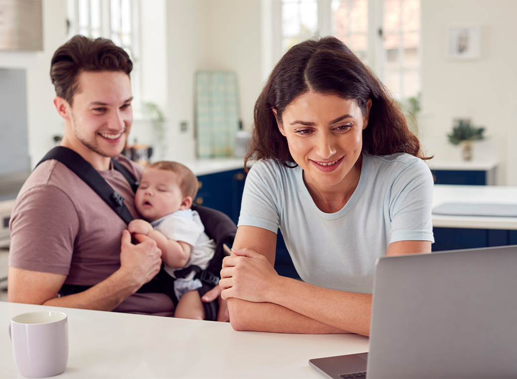 Happy young couple with their baby and laptop in the kitchen at home